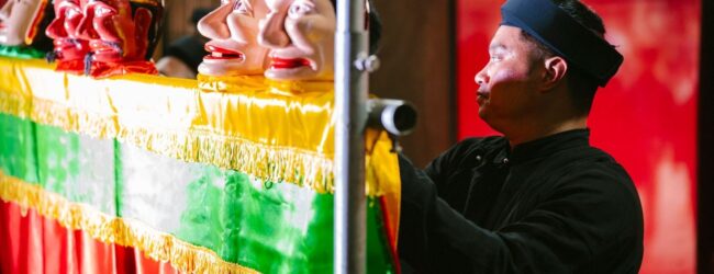Mustiin pukeutunut nukettaja ohjaa värikästä nukketeatterihahmoa